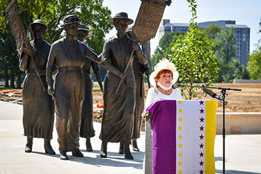 woman speaking at podium in front of suffragette monument