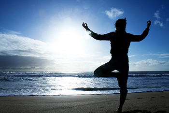 Picture of a person's silhouetted doing yoga on a beach.
