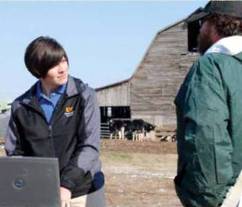 Young woman in the field talking to a farmer, while she is using a computer